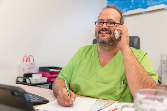 Mitarbeiter von Aktiv Dahoam lacht am Telefon im Büro München-Großhadern